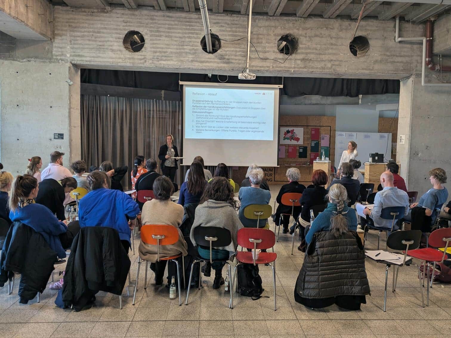 Das Foto zeigt ein Gruppe im Plenum sitzend während sie einer PowerPoint Präsentation folgen.